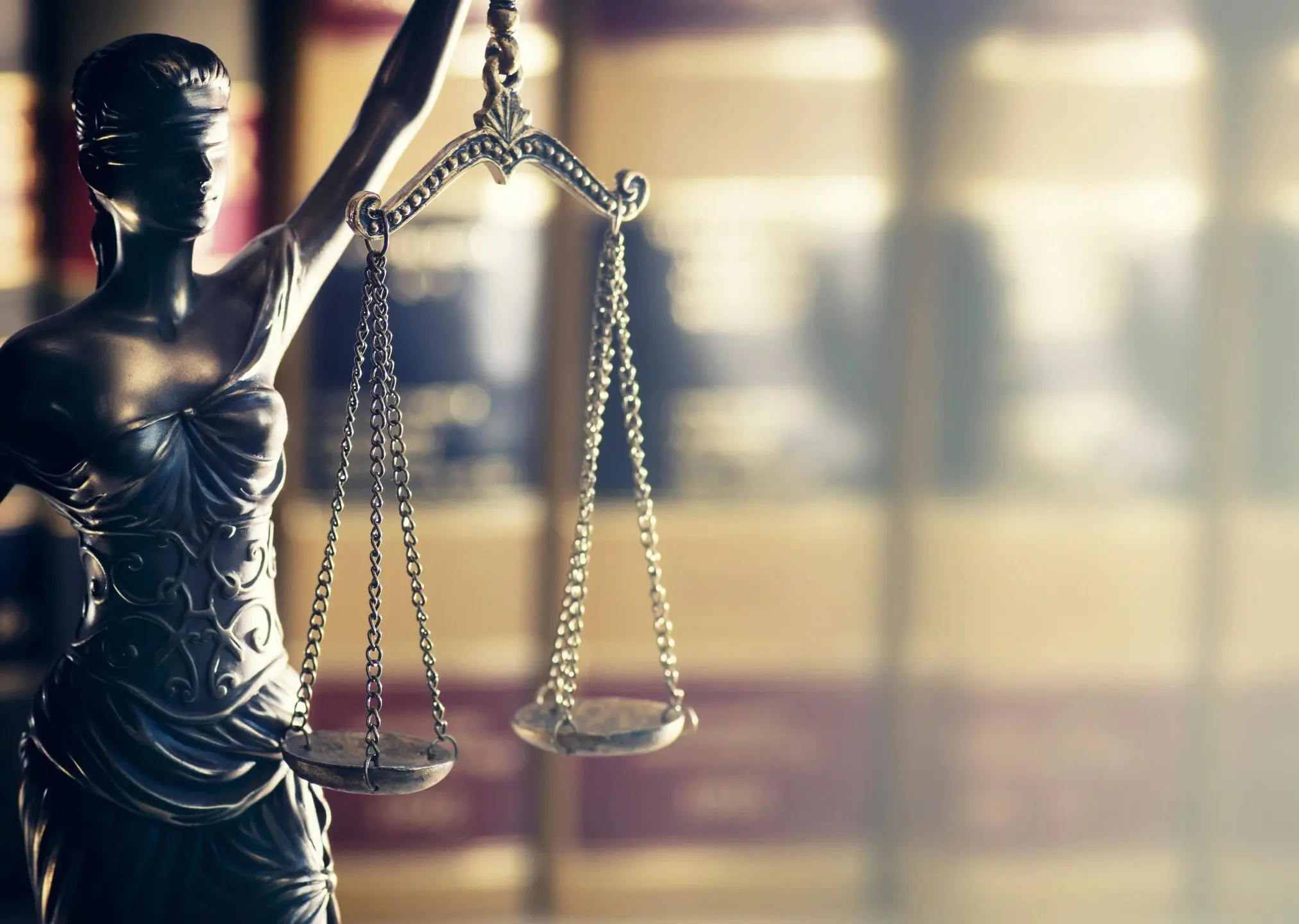 Close-up of Lady Justice statue holding scales against blurred courtroom background.